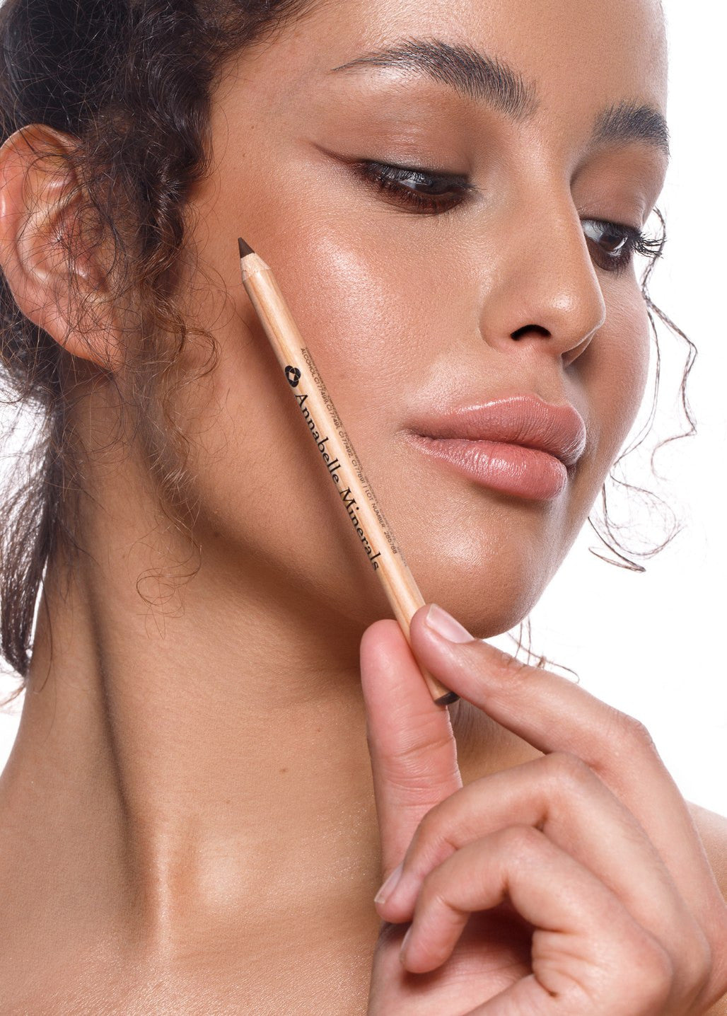Kobieta trzymająca brązową kredkę do oczu Annabelle Minerals przy twarzy