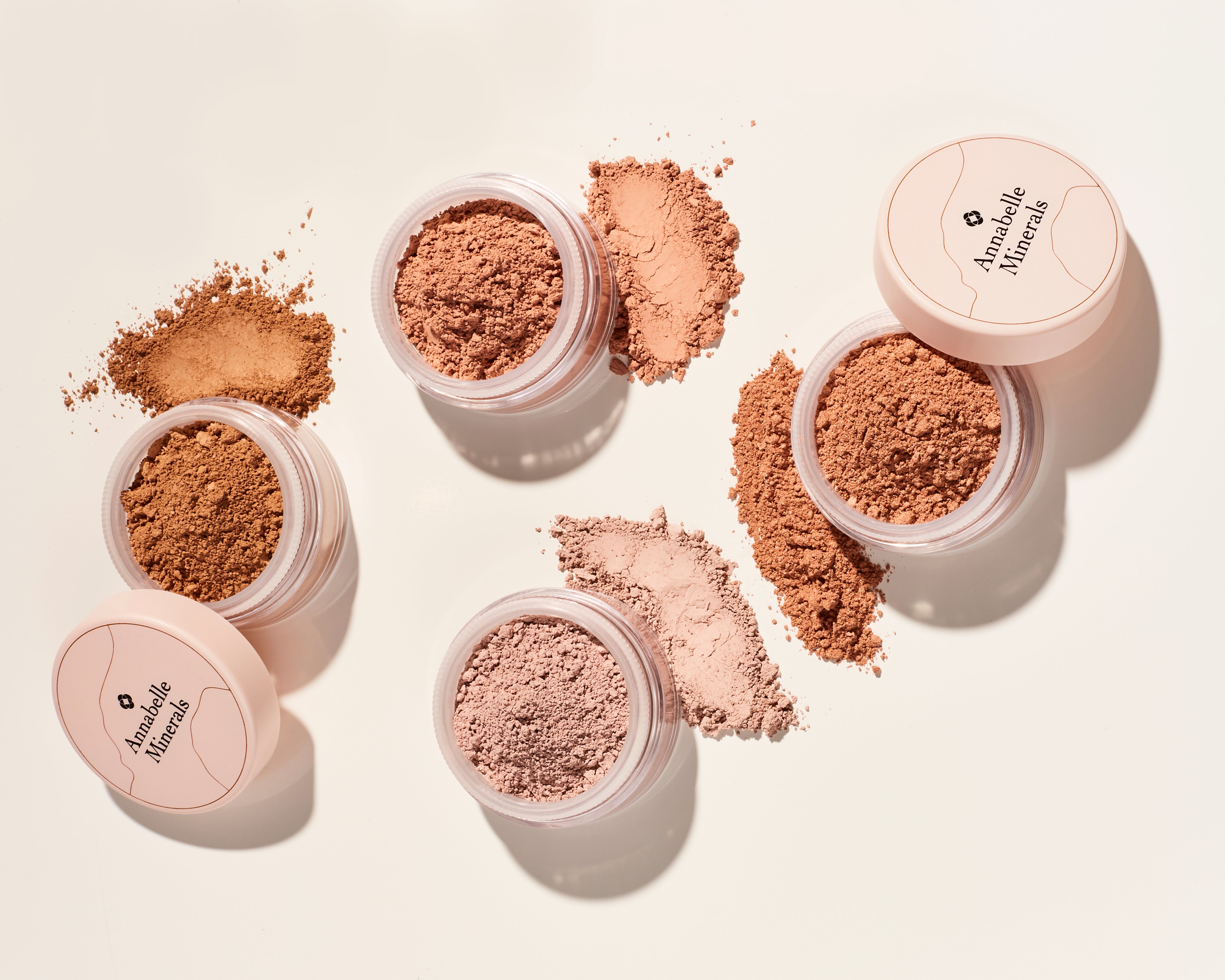 Podkłady mineralne Annabelle Minerals w różnych odcieniach, rozsypane obok słoiczków z etykietami