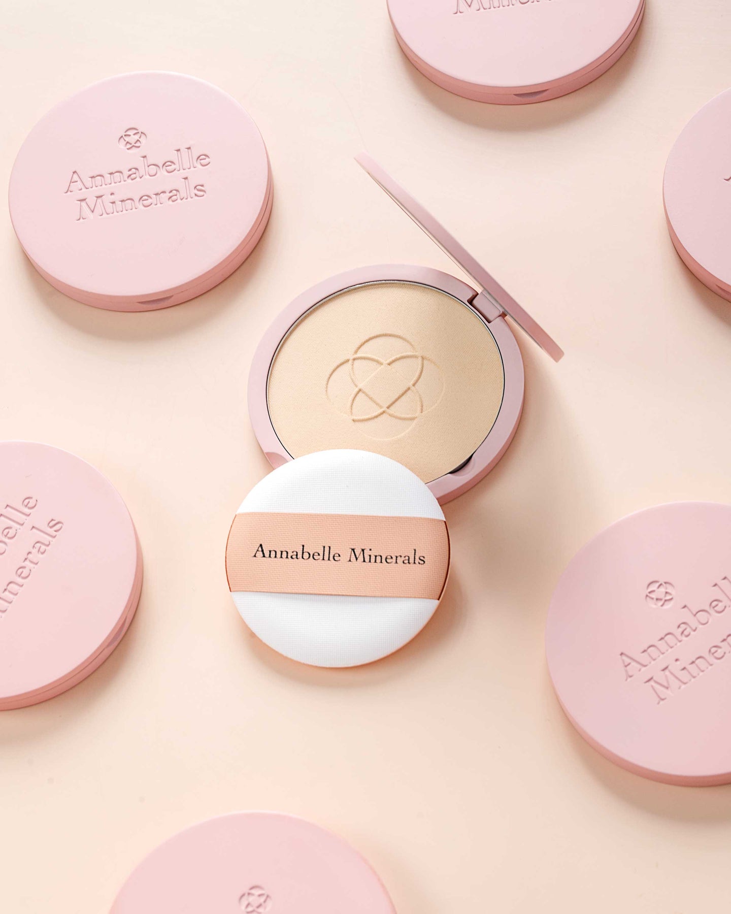 Otwarty podkład w kompaktowym opakowaniu w odcieniu beżu, otoczony zamkniętymi kosmetykami Annabelle Minerals