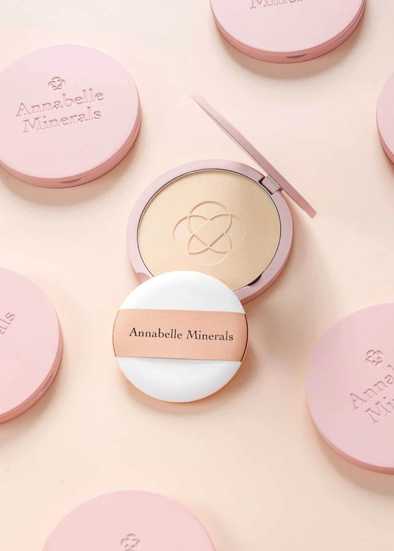 Kosmetyki Annabelle Minerals w minimalistycznych opakowaniach z różowym wykończeniem i aplikatorem do podkładu w kompakcie