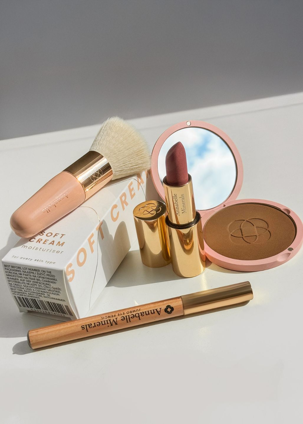 Różnorodne kosmetyki Annabelle Minerals: pędzel flat top, kompaktowy bronzer mineralny, szminka. krem Soft Cream i kredka do oczu w stylowej aranżacji