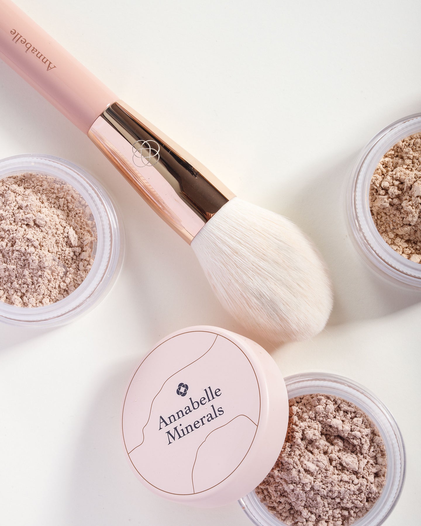 Różowy pędzel do pudru Annabelle Minerals obok pojemników z pudrami mineralnymi