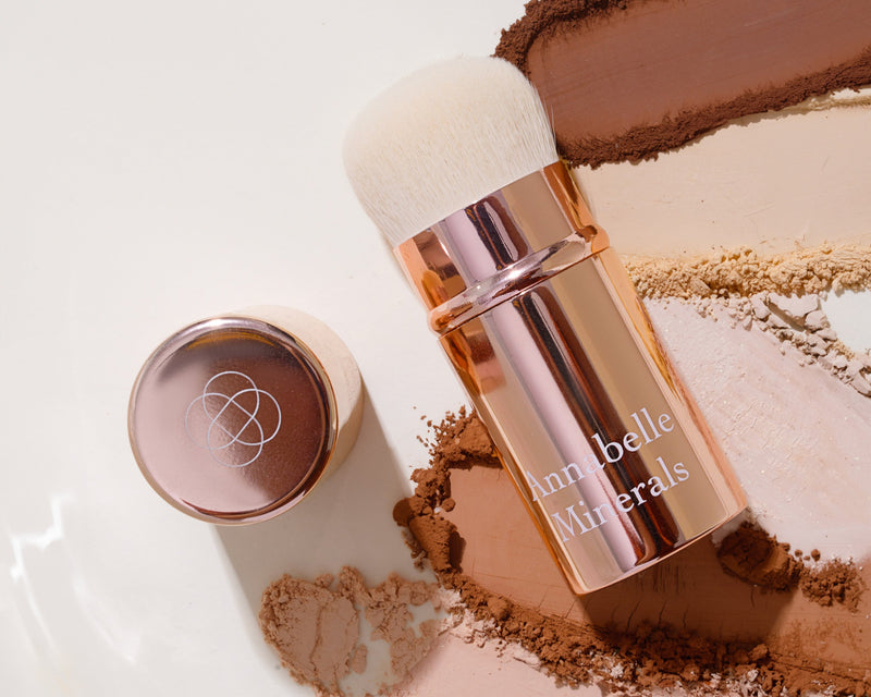 Pędzel z miękkim włosiem obok pojemnika z podkładem mineralnym w neutralnych odcieniach