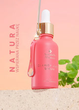 Różowa butelka serum Clarity Juice Annabelle Minerals z pipetą na tle gradientu i zielonymi liśćmi, z napisem NATURA WSPIERANA PRZEZ NAUKĘ