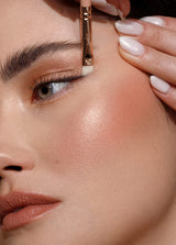 Kobieta nakłada makijaż, używając pędzla do eyelinera Annabelle Minerals, z zadbanymi paznokciami i gładką skórą