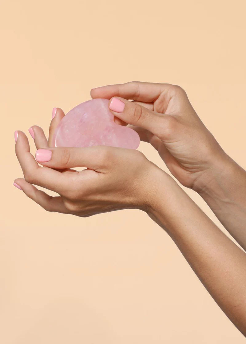 Różowy kamień gua sha trzymany w dłoniach z jasnoróżowym manicurem