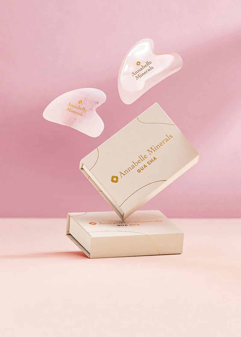 Kamienie gua sha unoszą się nad eleganckim pudełkiem na różowym tle