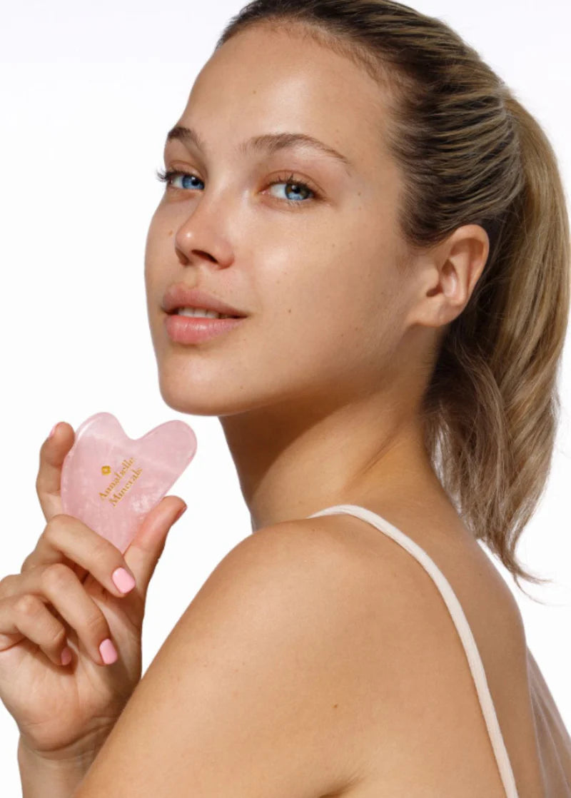 Młoda kobieta z kamieniem gua sha z naturalnego kwarcu na neutralnym tle, promująca naturalne podejście do pielęgnacji skóry