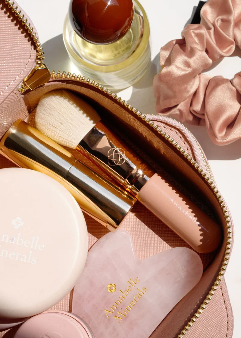 Różowa kosmetyczka z akcesoriami do makijażu Annabelle Minerals, w tym pędzel i mała buteleczka perfum
